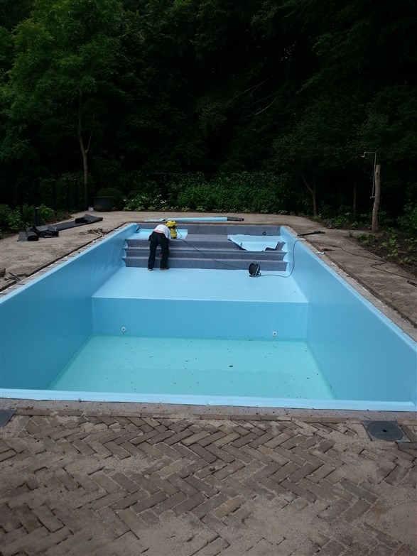 Leeg lichtblauw bassin met een vakman op de trap aan de kopzijde, bos erachter.