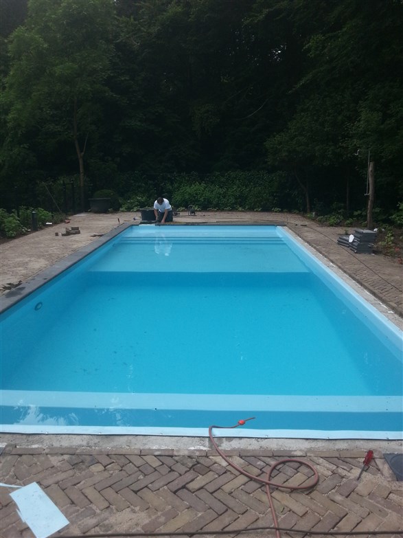 Gevuld bassin met lichtblauw water, trap aan de kopzijde en klinkerbestrating eromheen.