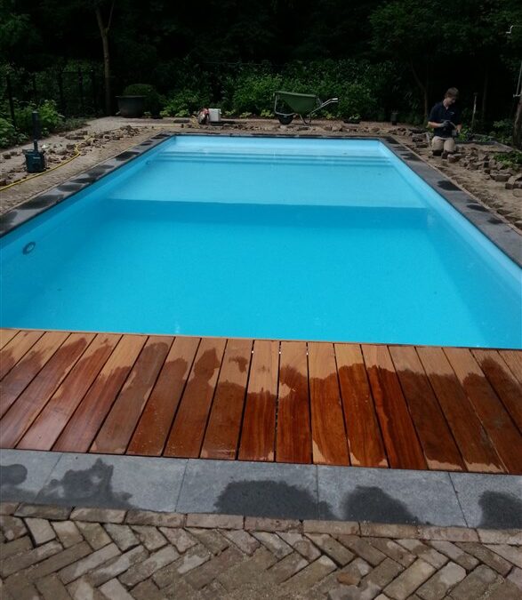Zwembad in Hilversum met lichtblauw water, houten vlonder en grijze randstenen, omringd door bos.