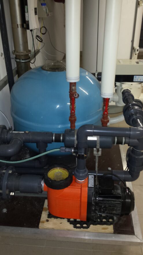 Blauwe filtertank met pomp en leidingwerk in de techniekruimte van het binnenzwembad.