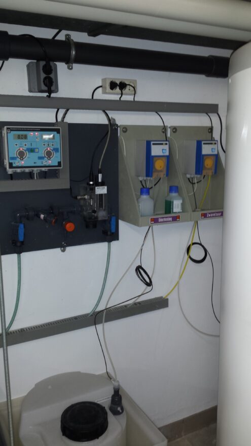 Wandpaneel met doseerpompen en meetapparatuur voor de waterzuivering in de techniekruimte.