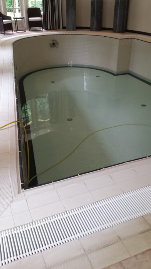 Binnenzwembad met grijsgroen water en wit rooster langs de rand, tijdens de renovatie in Blaricum.