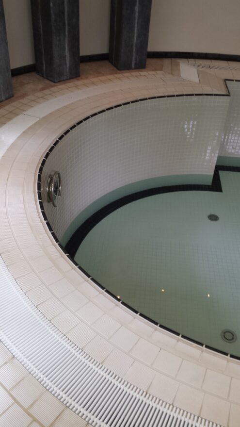 Halfronde kop van het binnenzwembad met lichte tegelrand, wit rooster en donker water.