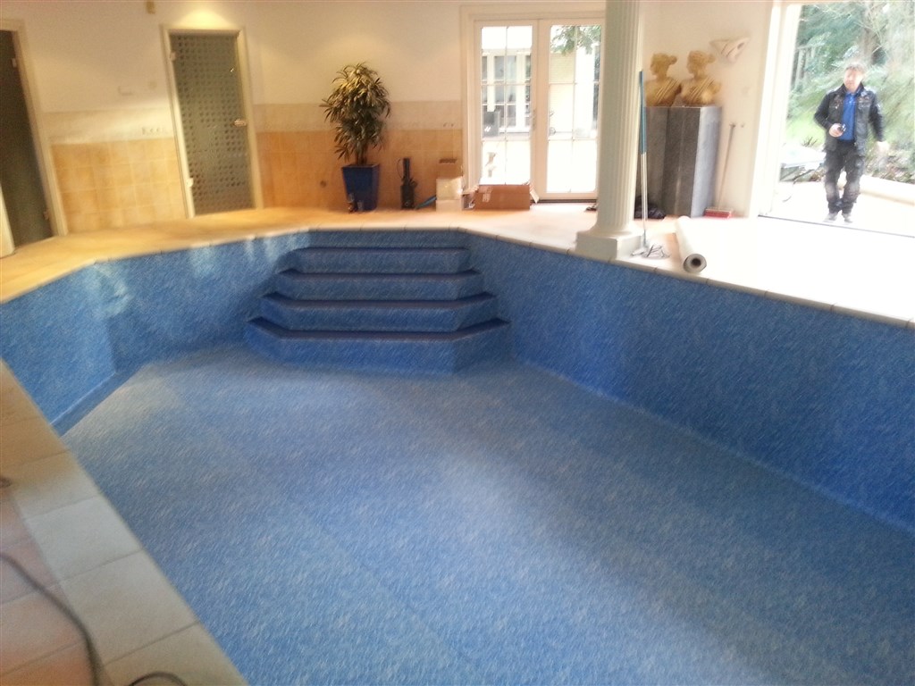 Bassin met blauwe folie op wanden, vloer en trap, vanaf het trapeinde gezien.