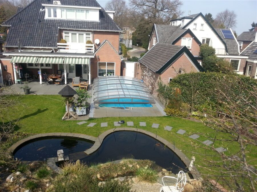 Tuin in Soest met een heldere overkapping over het zwembad, naast een vijver en stapstenen.