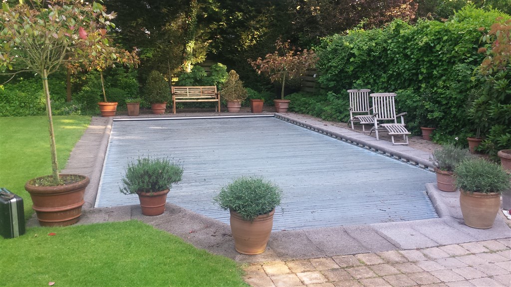 Zwembad in Zeist met een grijze afdekking, omringd door potplanten, een bank en tuinstoelen.