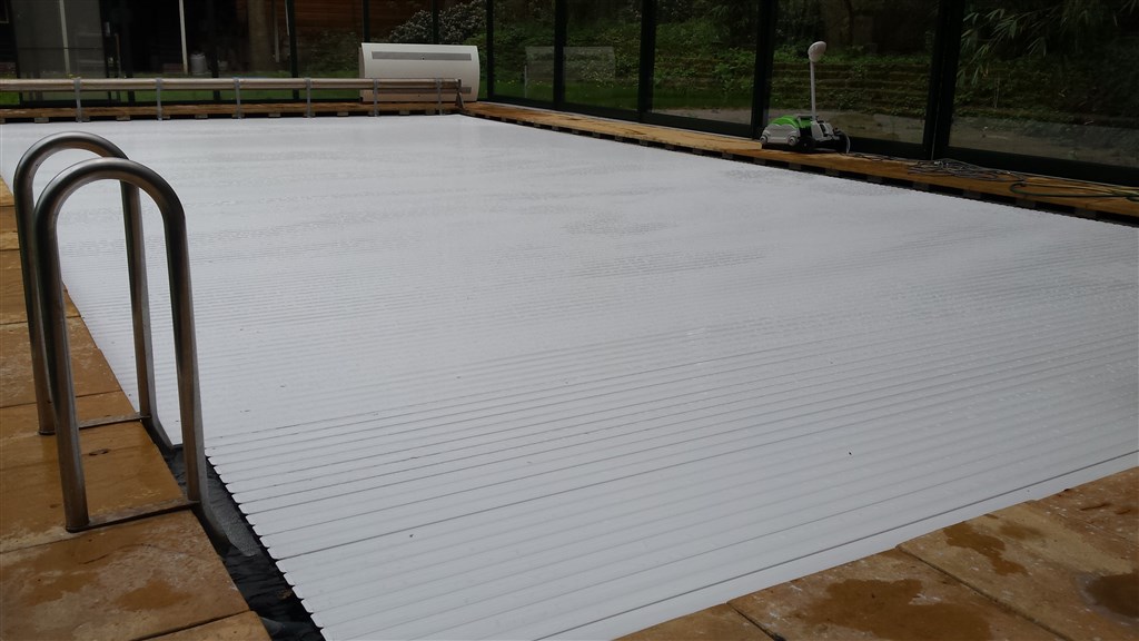 Gesloten witte lamellenafdekking over het binnenzwembad, met metalen trapleuning en glazen wand erachter.