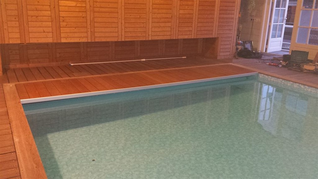 Houten vlonder langs de wand met een metalen stang, en helder water in het bassin.