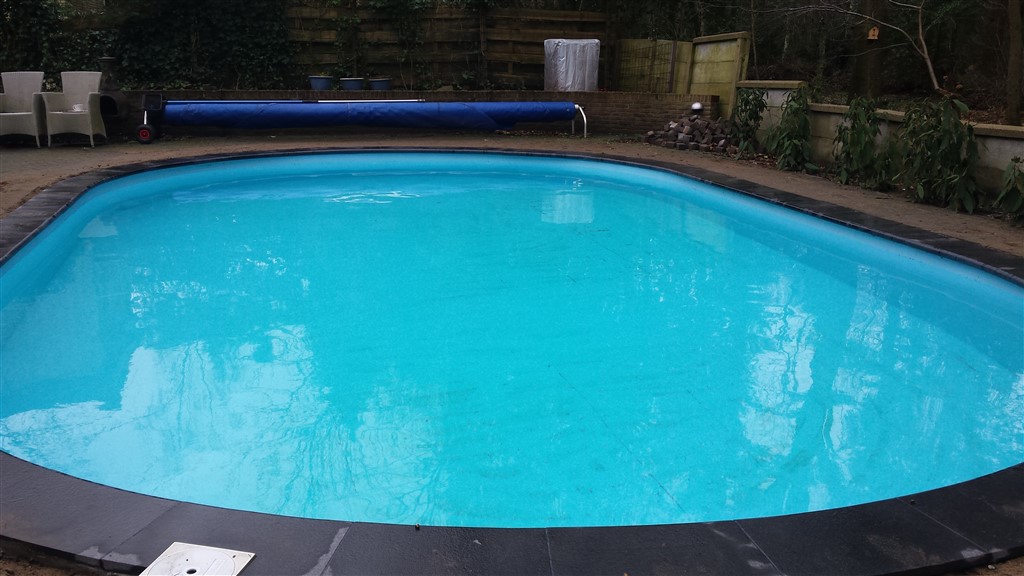 Zwembad met strakke zwarte rand en helderblauw water, tuinstoelen en opgerolde afdekking op de achtergrond.