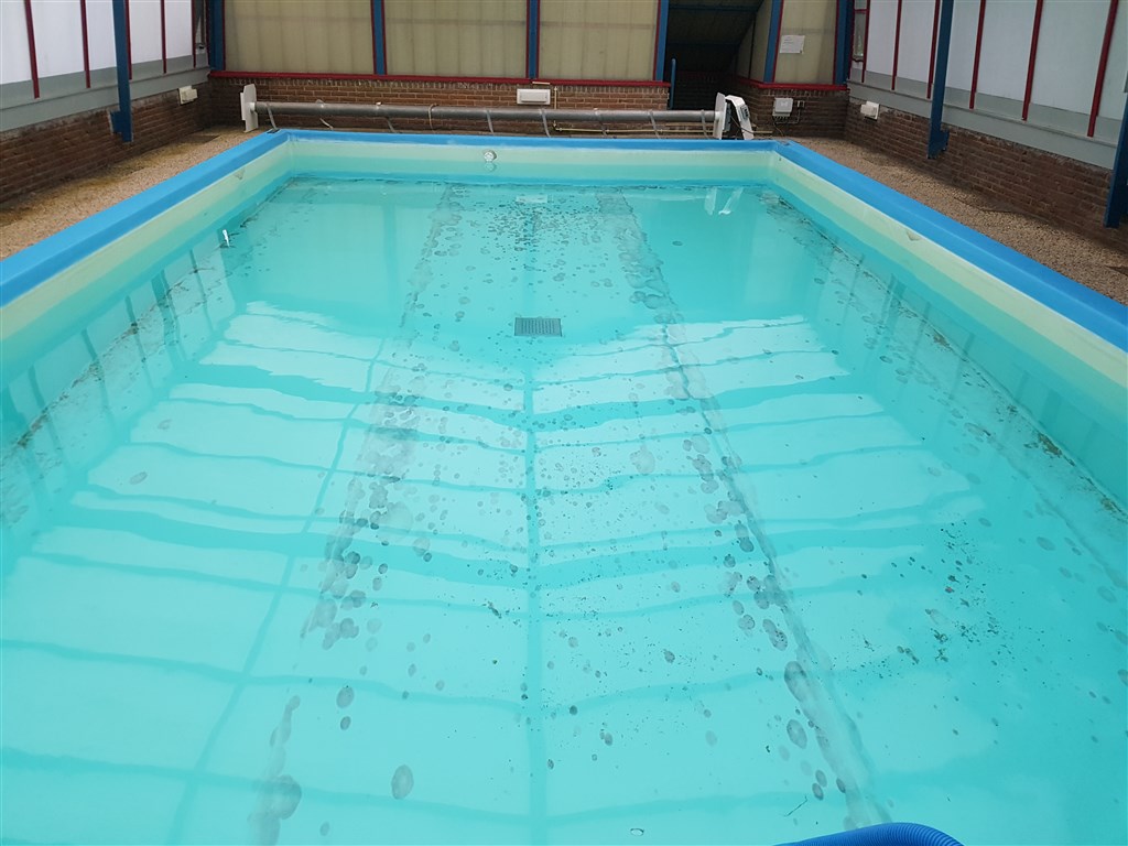 Turquoise bassin met verkleurde bodem vol vlekken en een blauwe rand, vóór de renovatie.