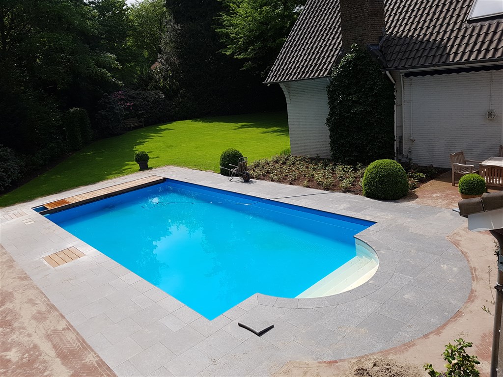 Afgewerkt bassin met ronde trap, grijze rand en gazon, in de tuin bij het woonhuis.