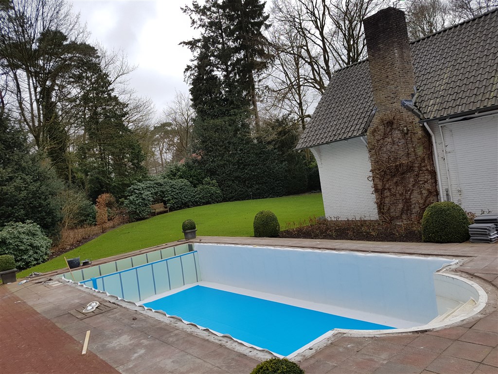 Bassin met witte wanden, blauwe bodem en ronde trapnis, met de tuin op de achtergrond.