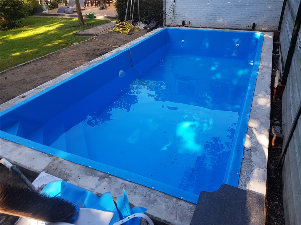 Bassin met nieuwe blauwe folie en water; de betonnen rand is nog onafgewerkt.