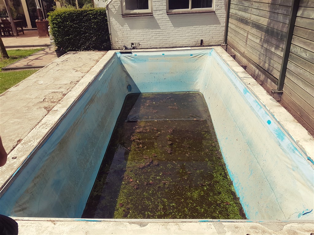 Oud bassin met groene aanslag op de bodem en verbleekte lichtblauwe folie, vóór de renovatie.