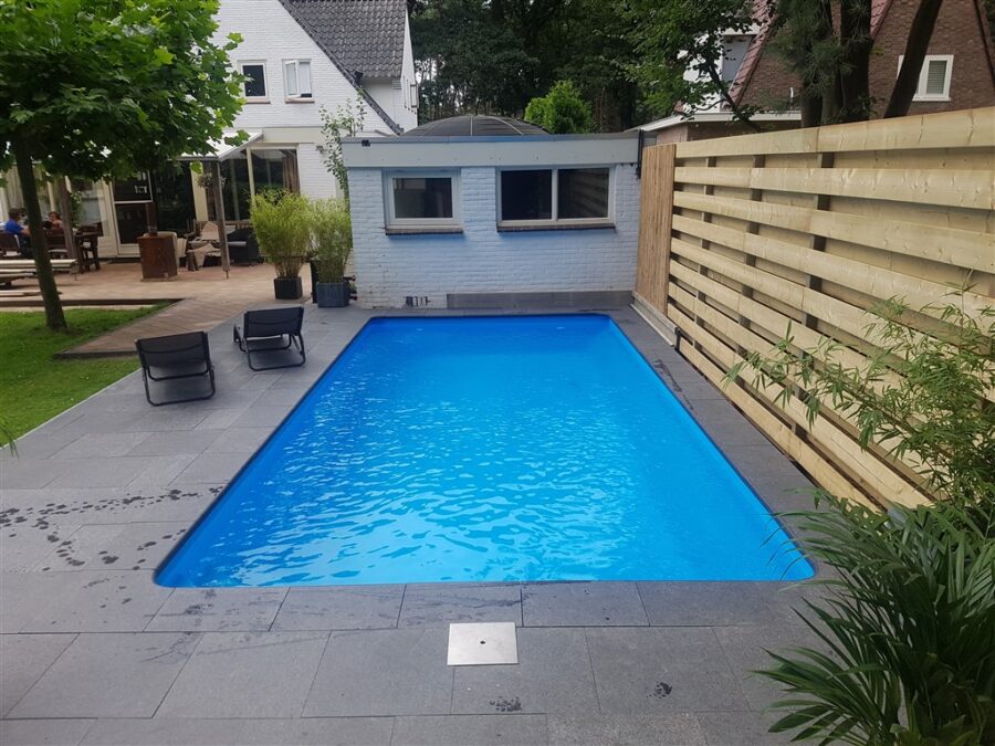Afgewerkt zwembad met blauwe folie, donkere stenen rand en twee ligstoelen voor een lichte houten schutting.