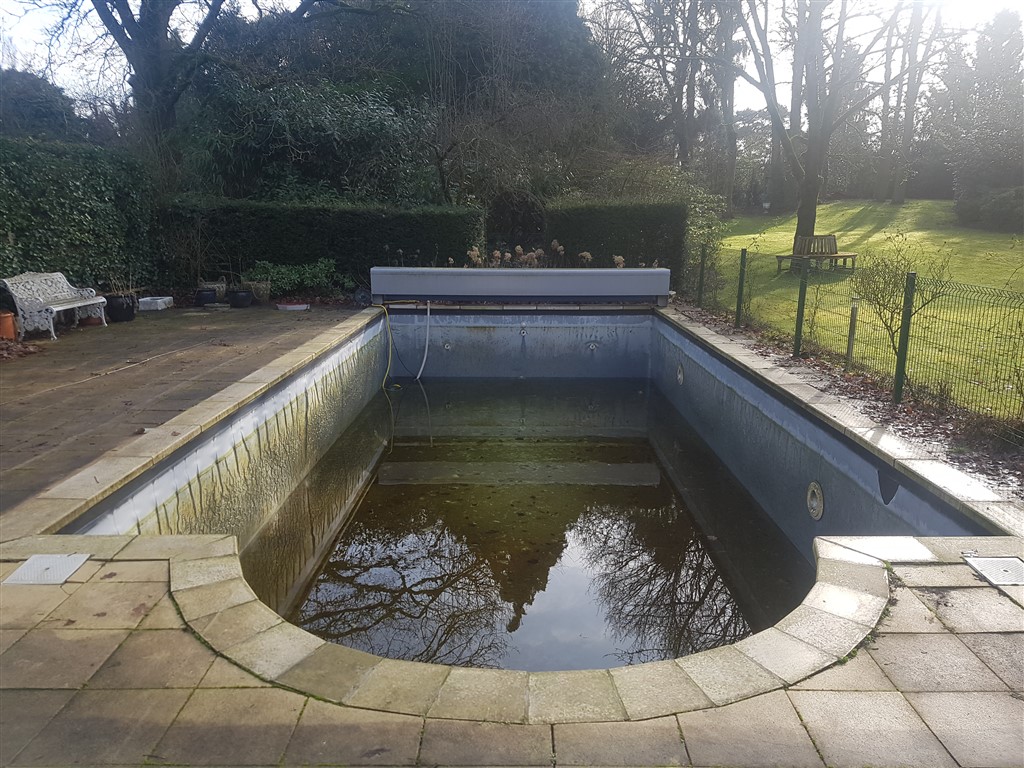 Oud bassin met donker water, gezien vanaf de ronde trap, met een bank links.