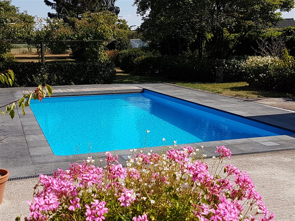 Afgewerkt zwembad in Soest met blauwe folie, grijze tegelrand en roze bloemen op de voorgrond.