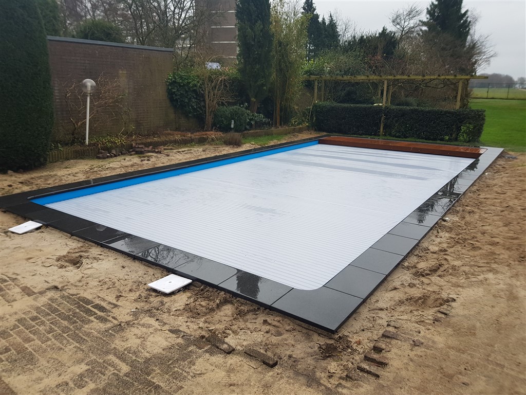 Zwembad met gesloten lamellenafdekking en een houten strook, het terras is nog zand.