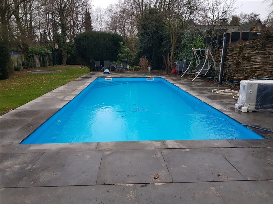 Helderblauw zwembad met terras van grijze tegels in een tuin in Hollandsche Rading.
