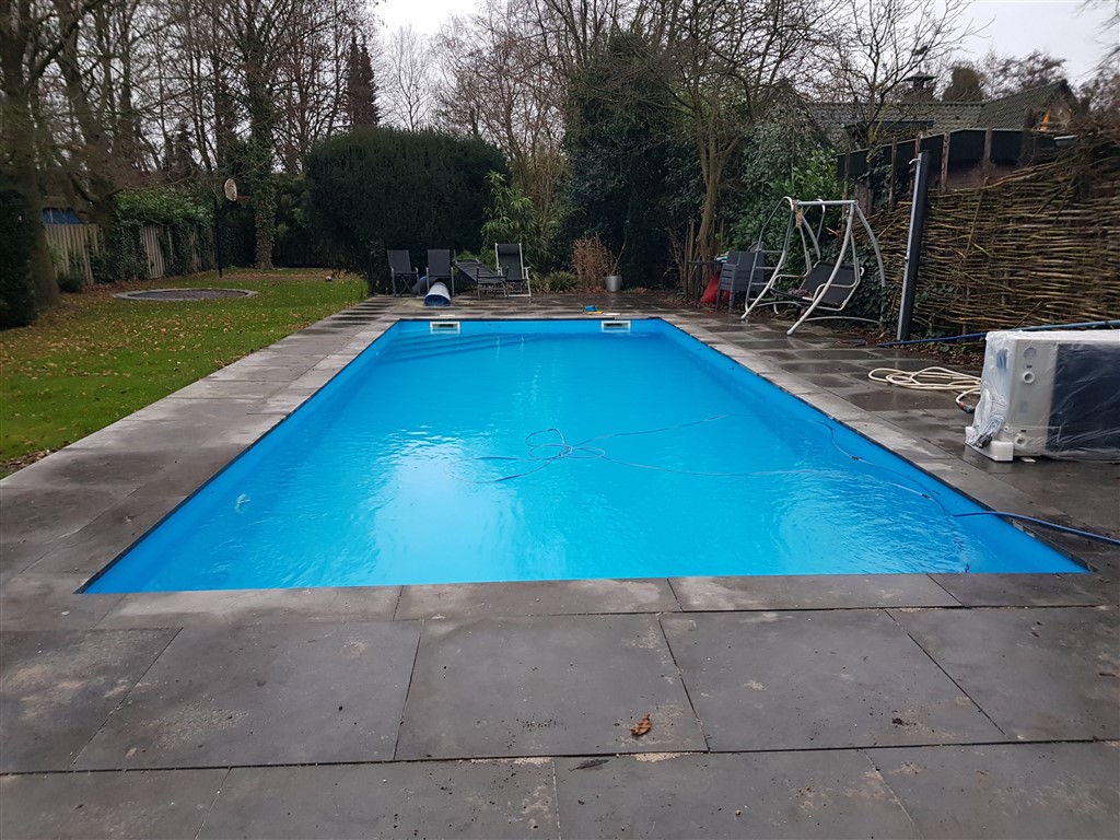 Helderblauw zwembad met terras van grijze tegels in een tuin in Hollandsche Rading.