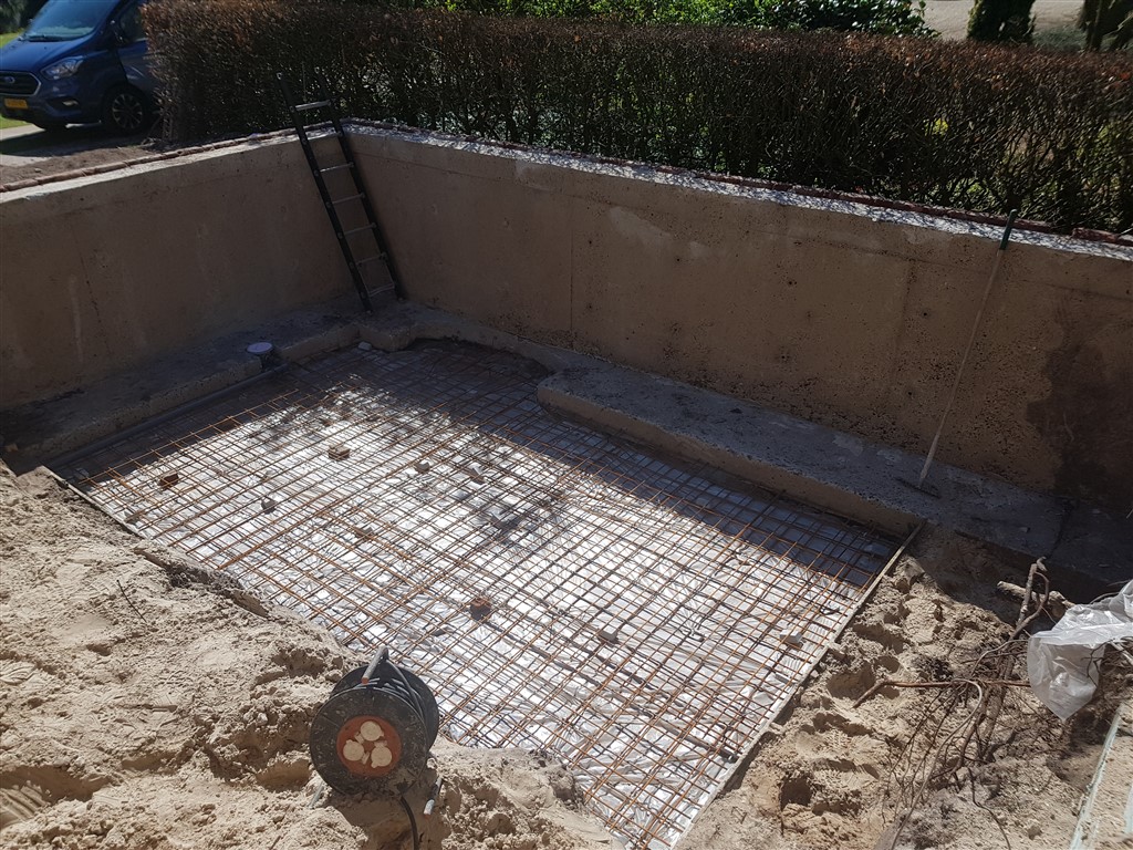 Wapeningsmat op de bodem van het uitgegraven bassin, met een ladder tegen de wand.