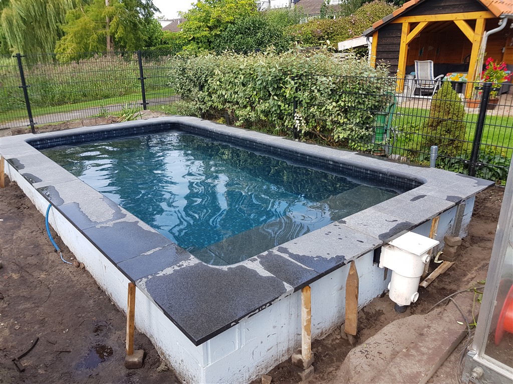 Natuurstenen rand rond het gevulde bassin, met witte wand en houten steunen eronder.