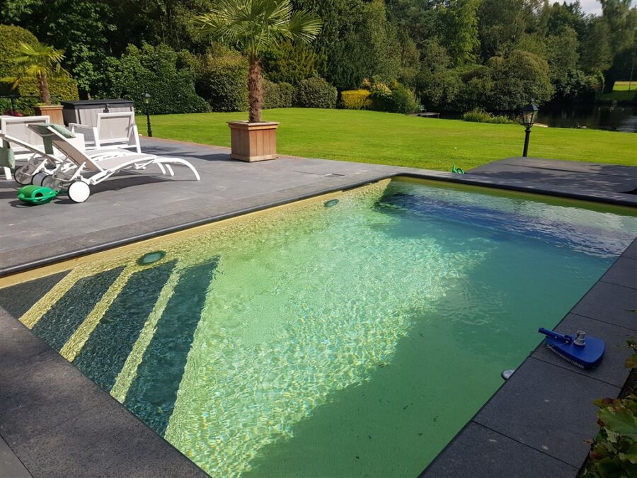 Gevuld bassin met trap in de hoek, natuurstenen rand en grote grijze terrastegels, Den Dolder.