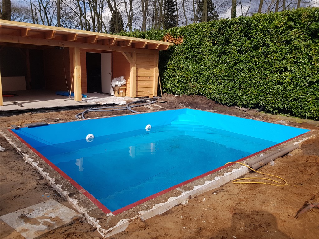 Het bassin met blauwe folie is gevuld met water, nog zonder rand eromheen.