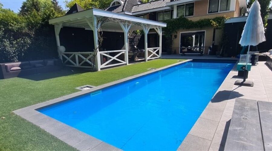 Blauw zwembad met tegelrand langs het gazon, met wit tuinprieel en parasol in Soest.