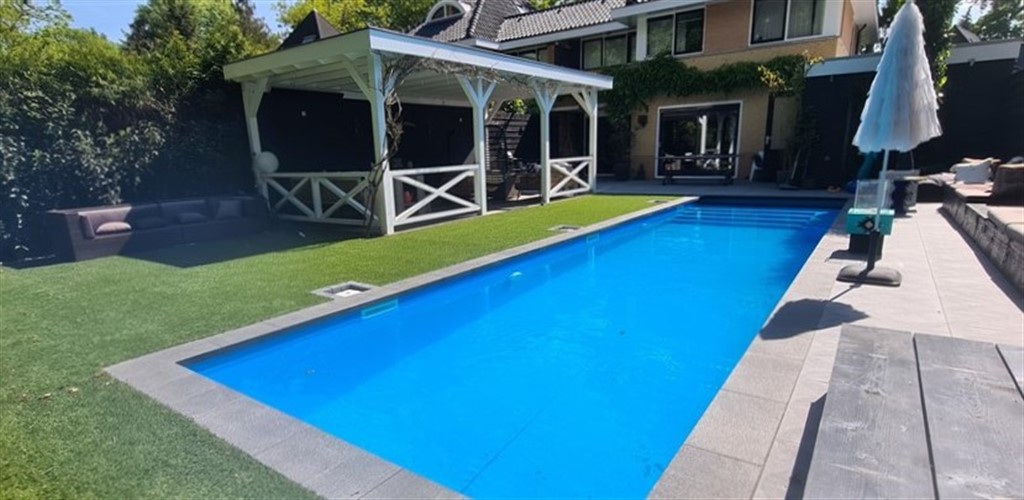 Blauw zwembad met tegelrand langs het gazon, met wit tuinprieel en parasol in Soest.