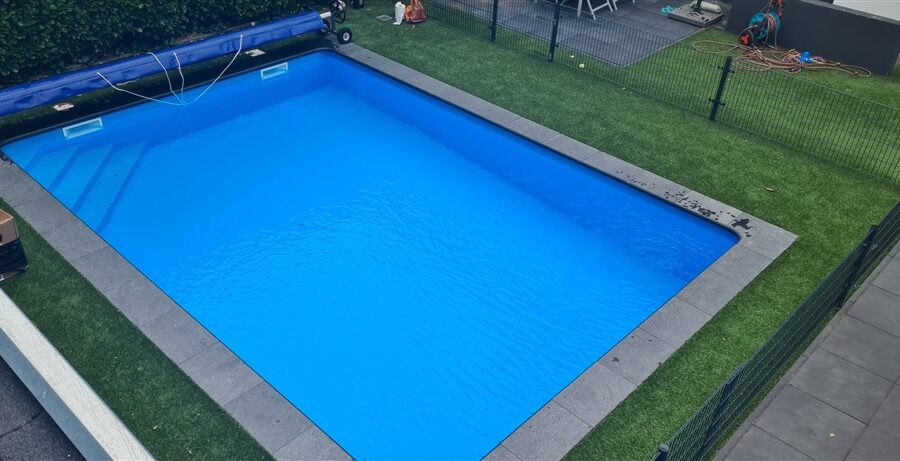 Opgeleverd bassin met blauwe folie en grijze natuurstenen rand in het gazon in Soest.