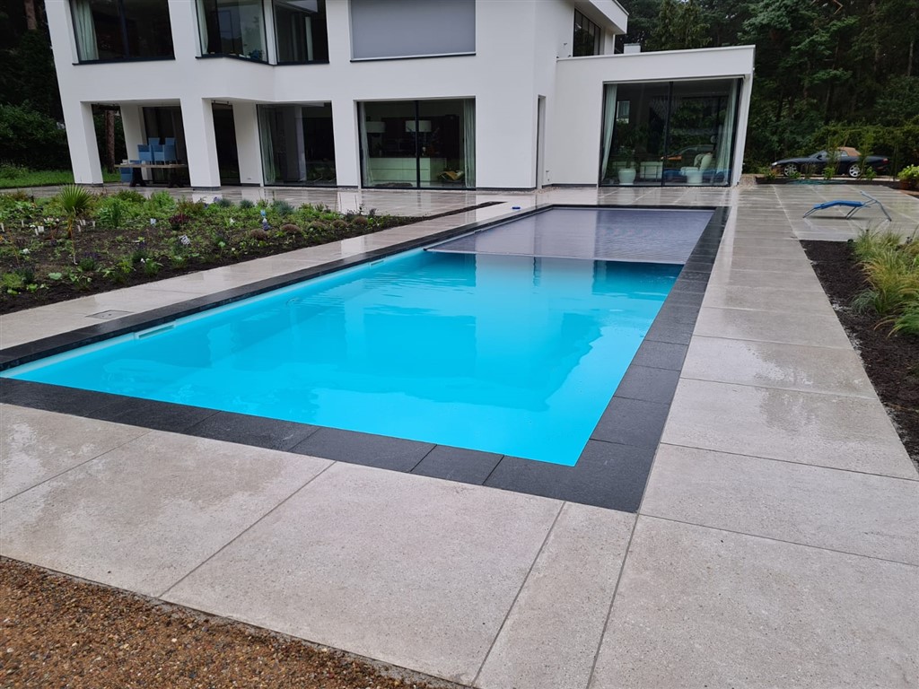Zwembad met donkere rand en lichte terrastegels bij een moderne villa in Bosch en Duin.