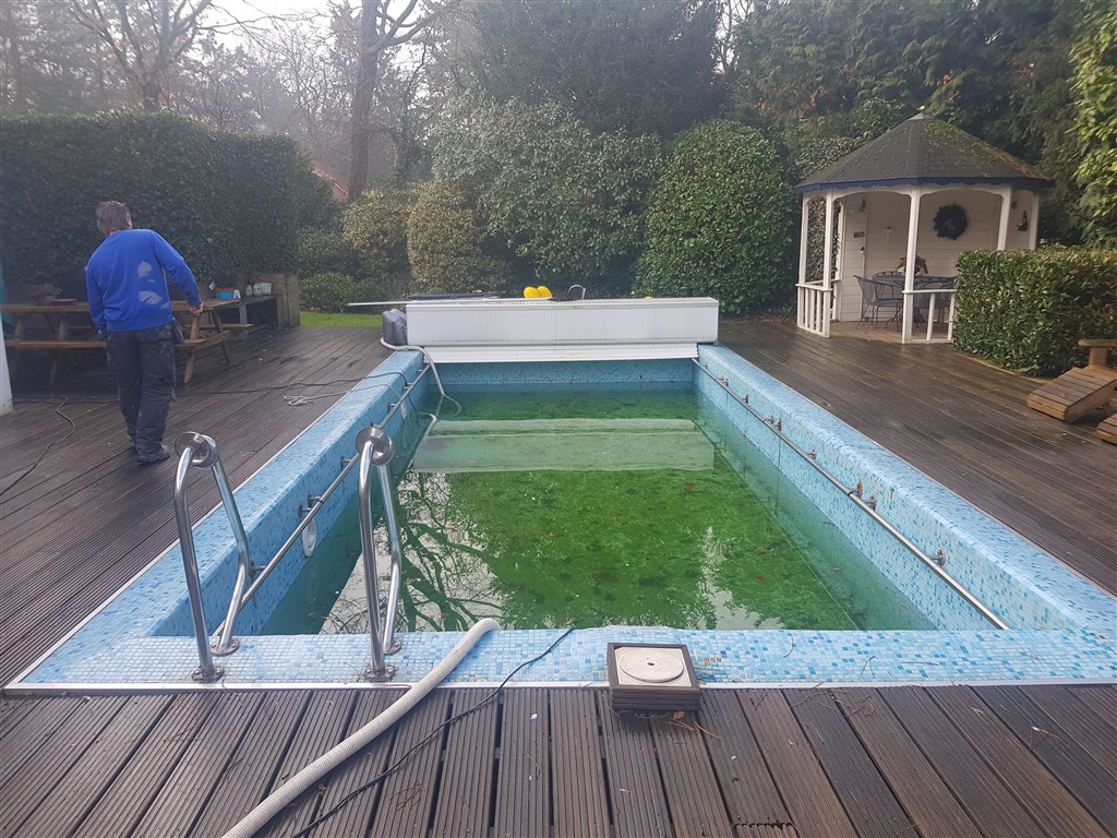 Het oude bassin met groen water en mozaïek, gezien vanaf de kop, met het tuinhuisje erachter.
