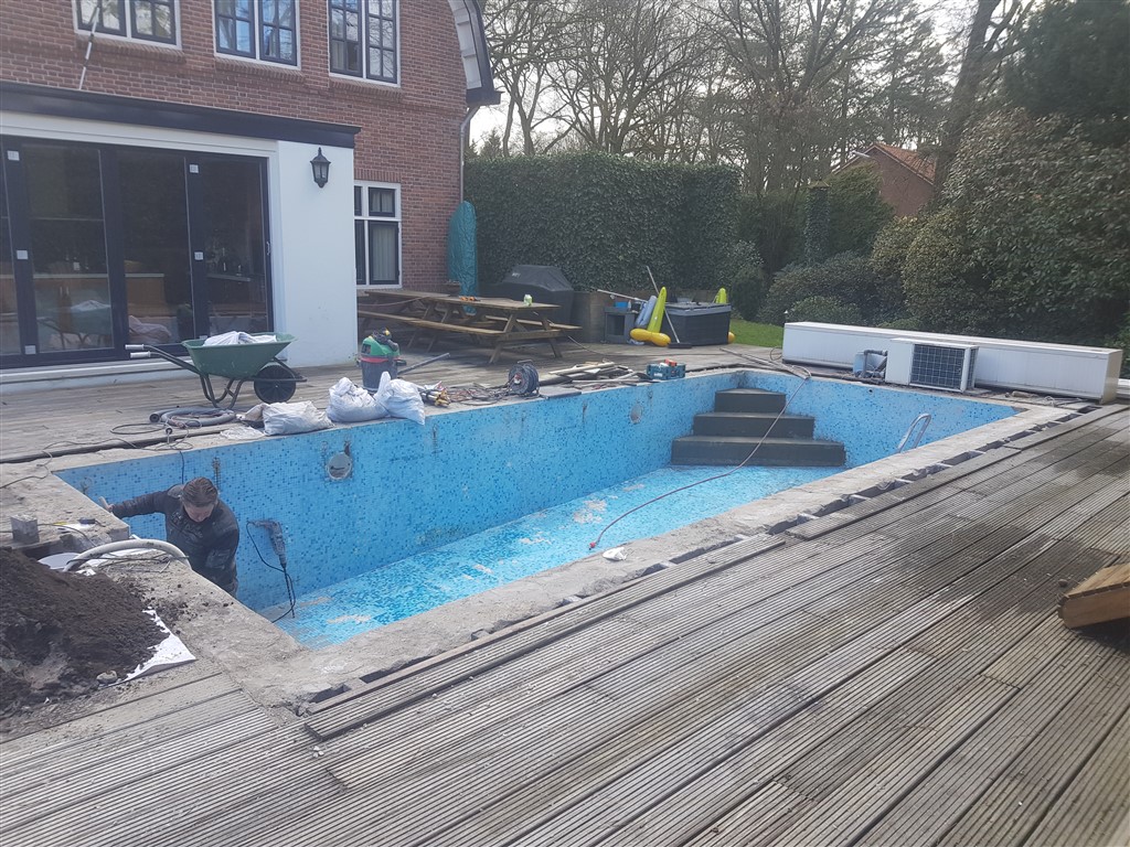 Het leeggemaakte bassin met oude blauwe mozaïektegels en een trap, tussen de houten vlonder.