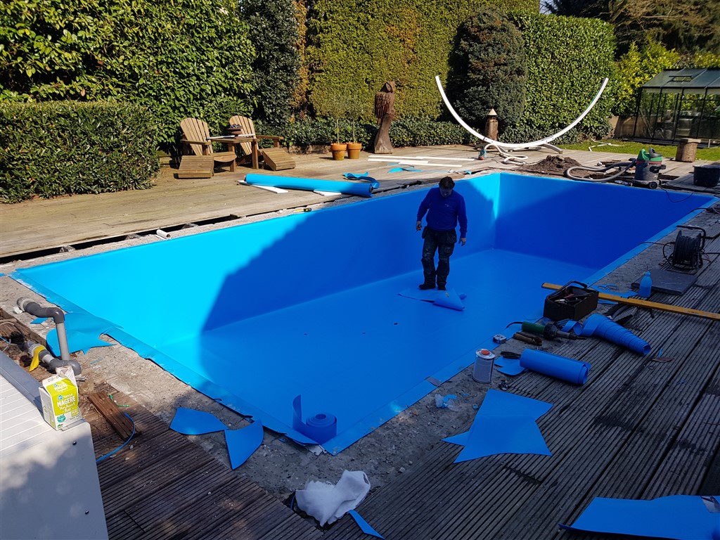 Een man staat op de blauwe folievloer van het bassin, met folieresten langs de rand.