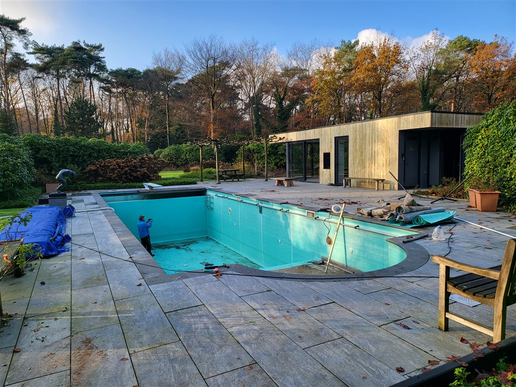 Het oude bassin met turquoise wanden en afgeronde hoek, in een terras van grote tegels.