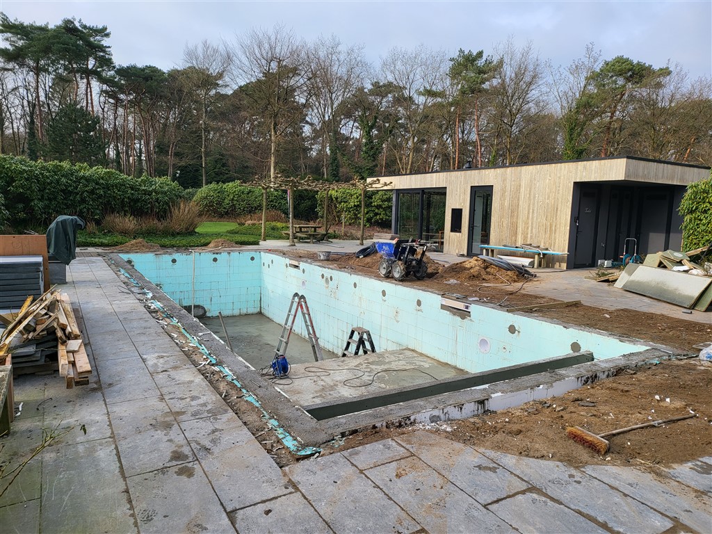 Het kale bassin met oude turquoise tegelwanden, ladders en terrastegels, voor het moderne tuinhuis.